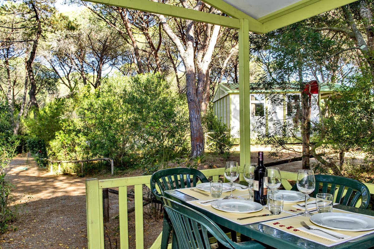An outdoor dining area with a table set for four, surrounded by greenery and trees.