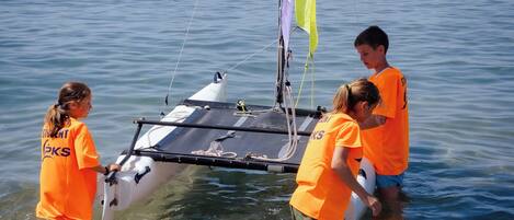 A small sailboat with a sail, being handled by people in orange shirts.