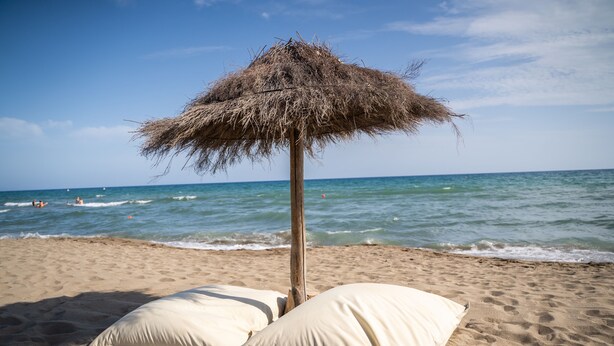 A beach with a thatched umbrella and two pillows on the sand. - Camping Maremma Sans Souci (Castiglione della Pescaia)