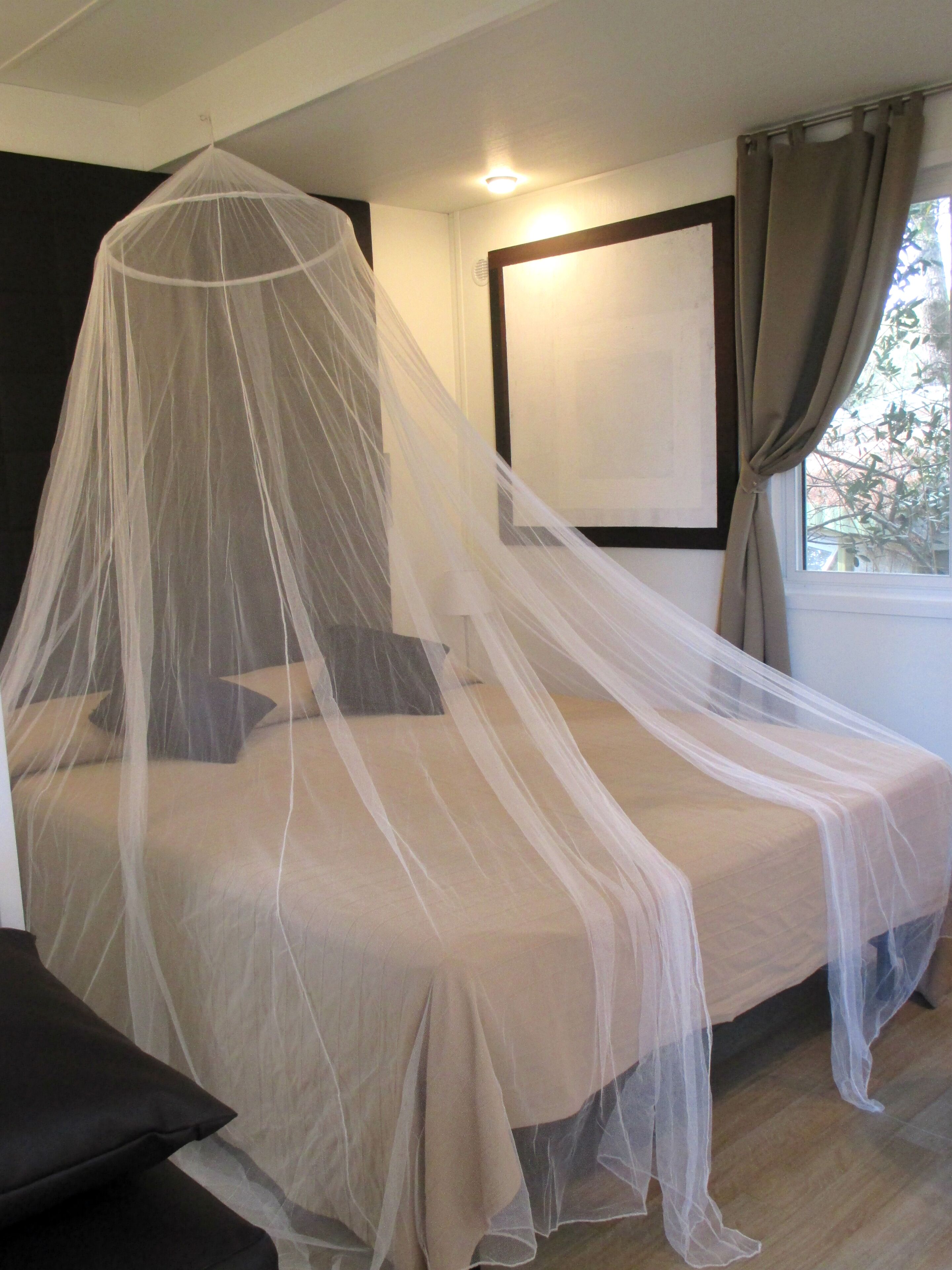 A bed with a canopy, a bedside table, and a window with curtains.