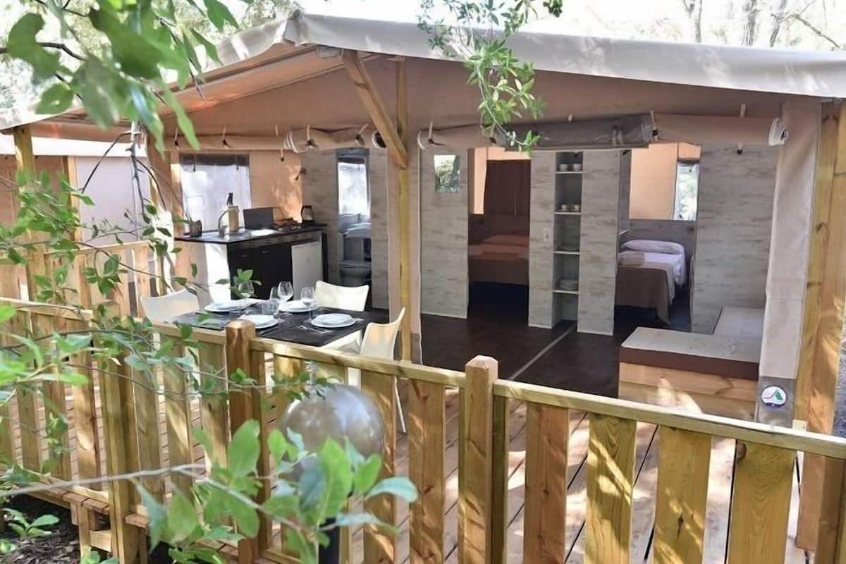 A cozy outdoor dining area with a wooden deck, a covered seating area, and a kitchen visible through the open sides.