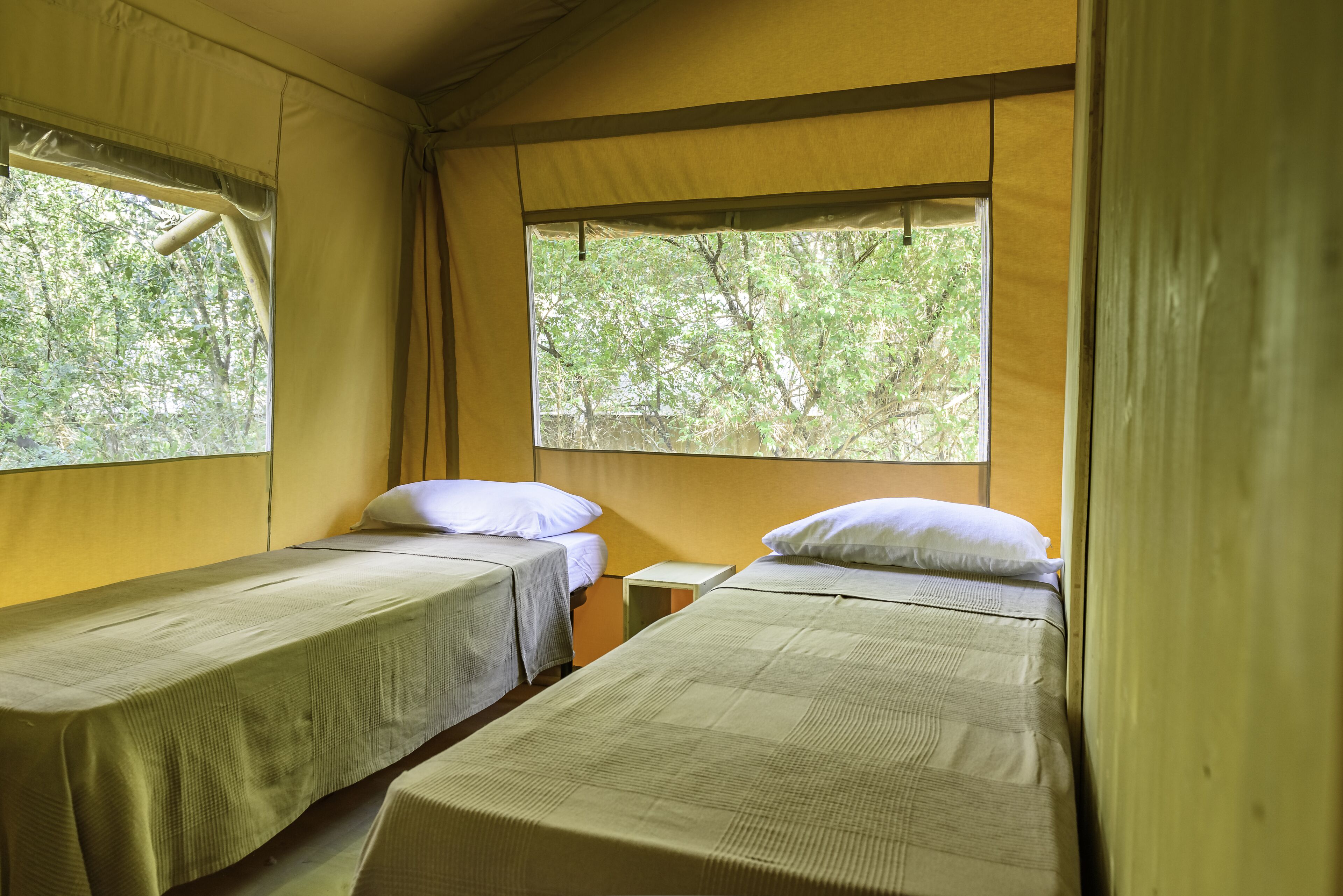 A room with two single beds, each with a pillow and a small bedside table.