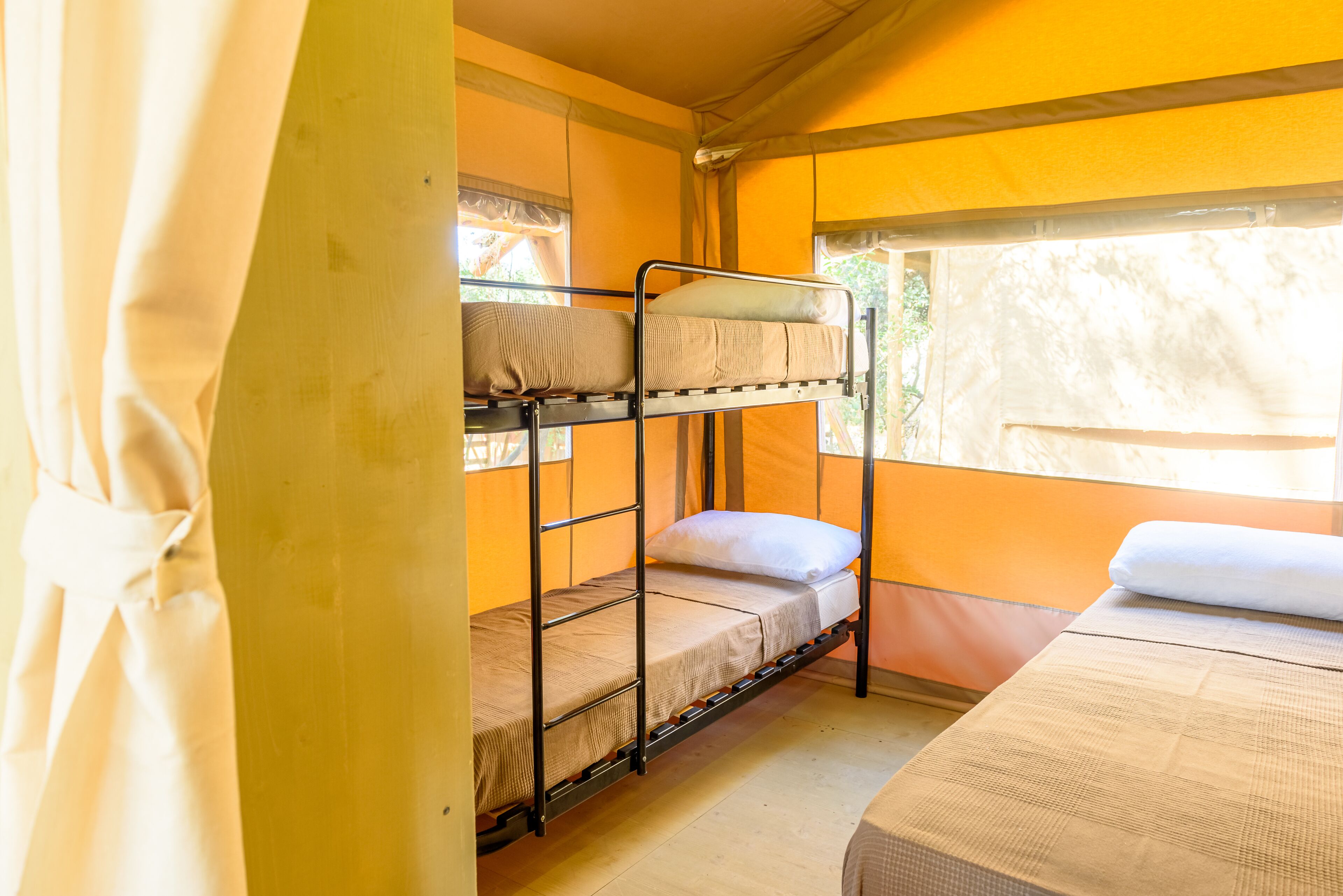 A bunk bed room with a window, curtains, and a bed with a blanket.