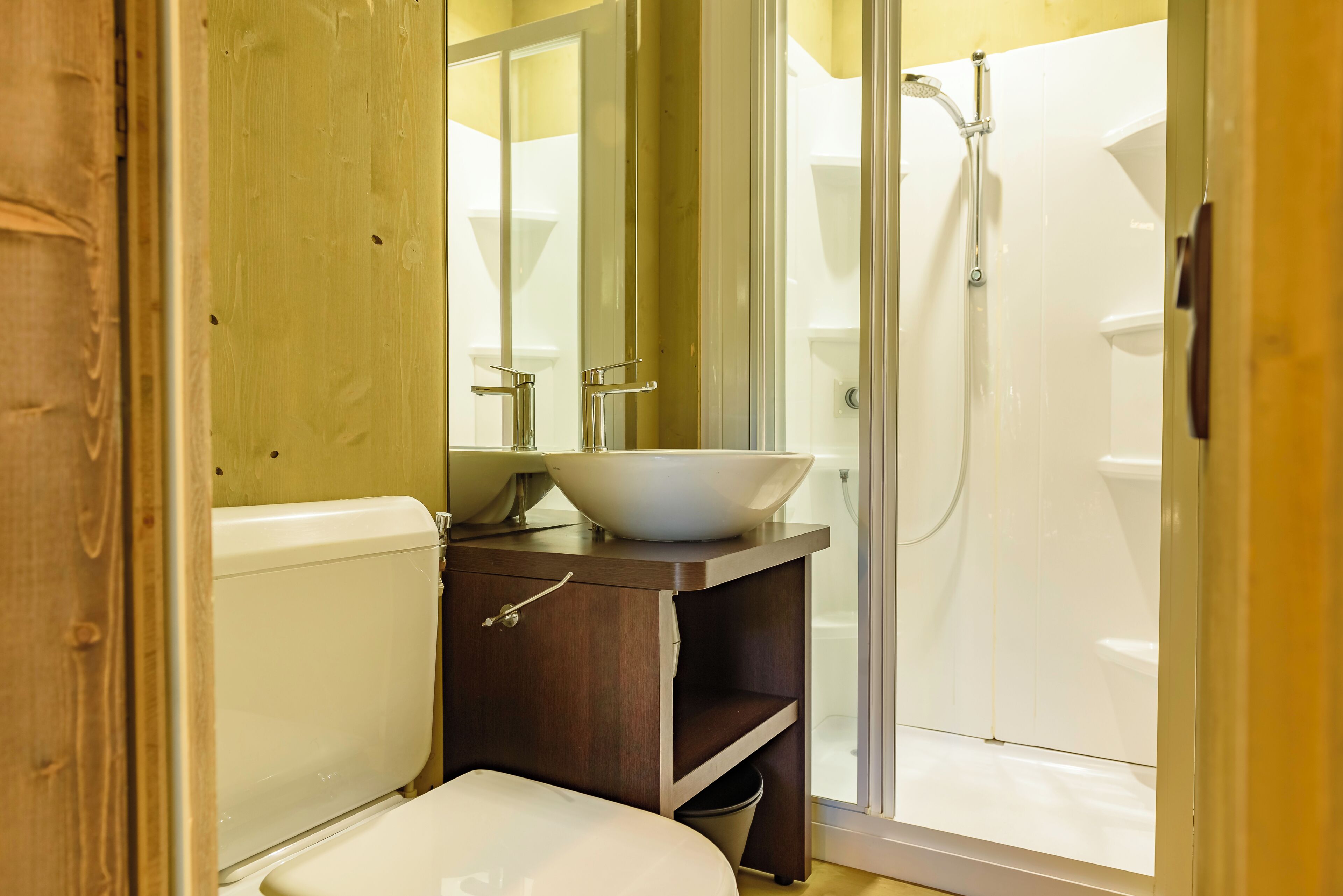 Un baño con tocador de madera, lavamanos blanco y cabina de ducha de vidrio.