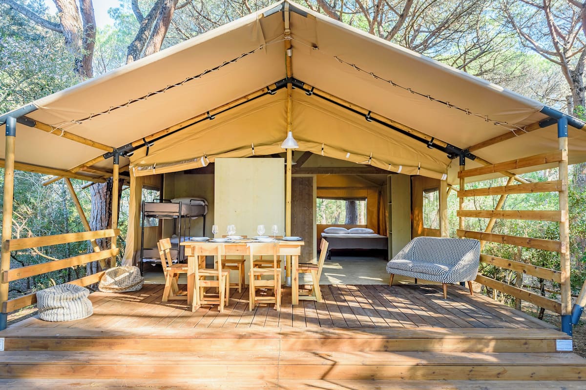 A wooden deck with a tented structure, a dining table with chairs, a sofa, and a bed.
