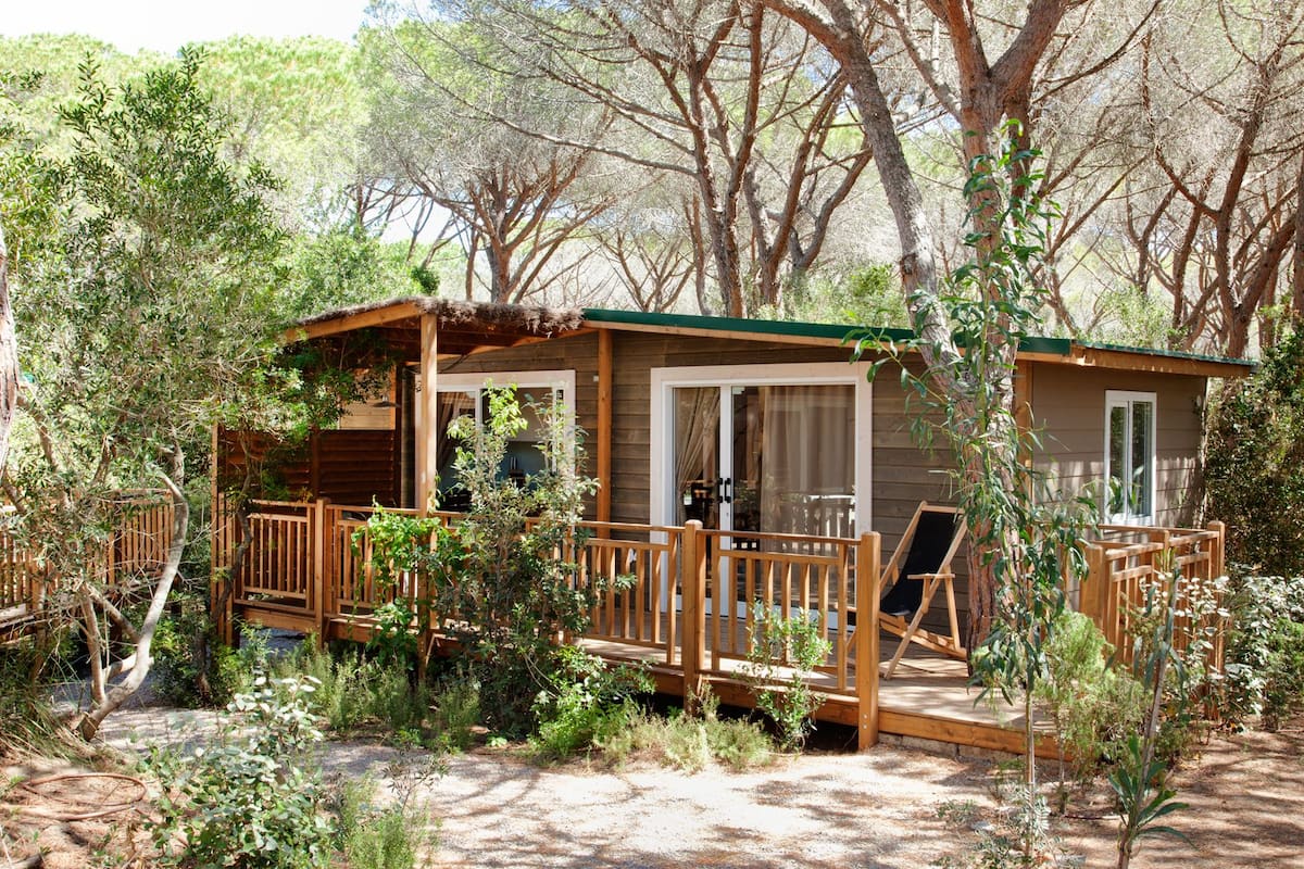 A wooden cabin with a deck, surrounded by trees and vegetation.