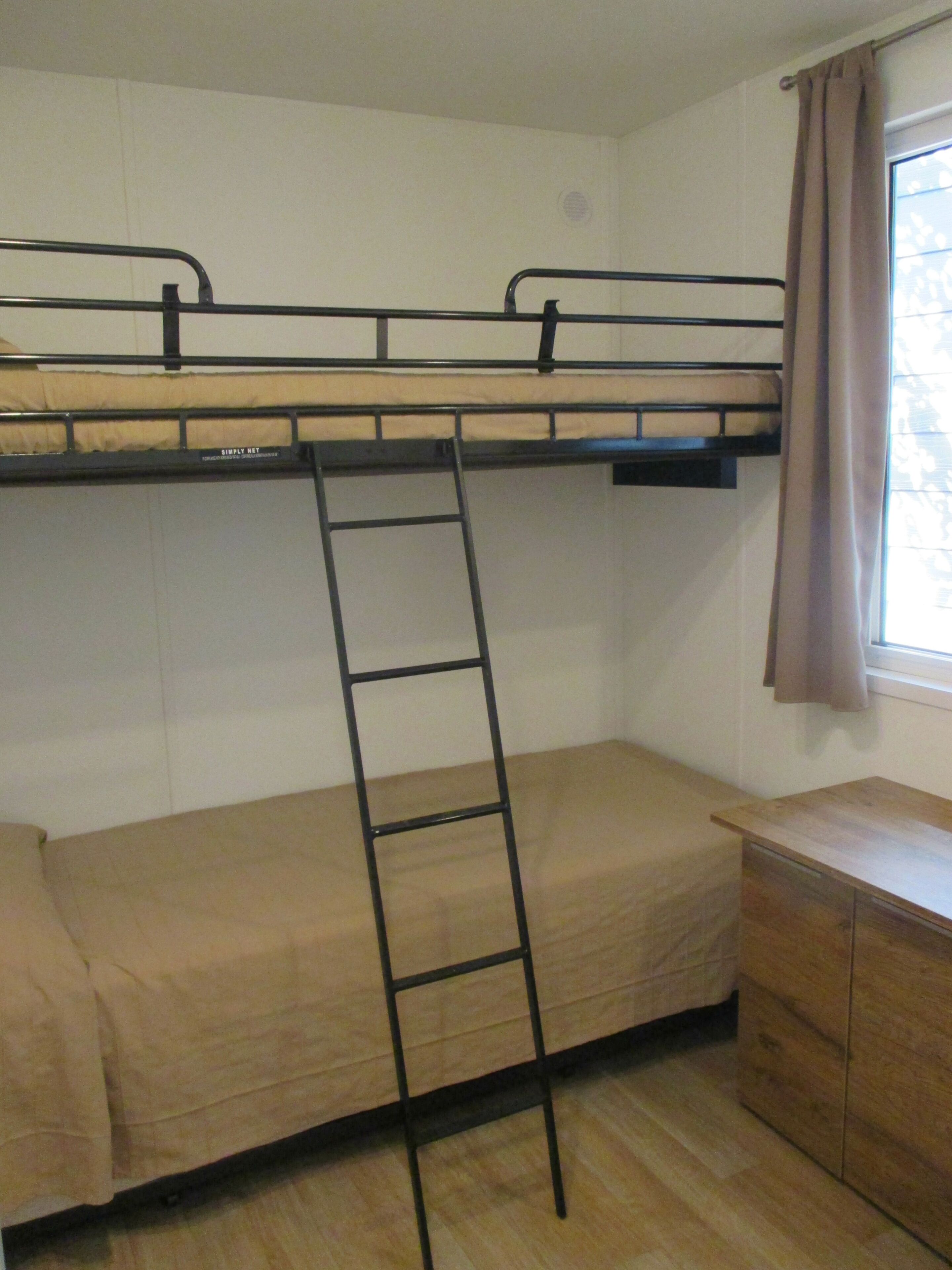 A bunk bed with a ladder, a wooden desk, and a window with curtains.