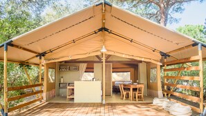 A wooden deck with a covered seating area, a table, and a bench. - Camping Maremma Sans Souci (Castiglione della Pescaia)
