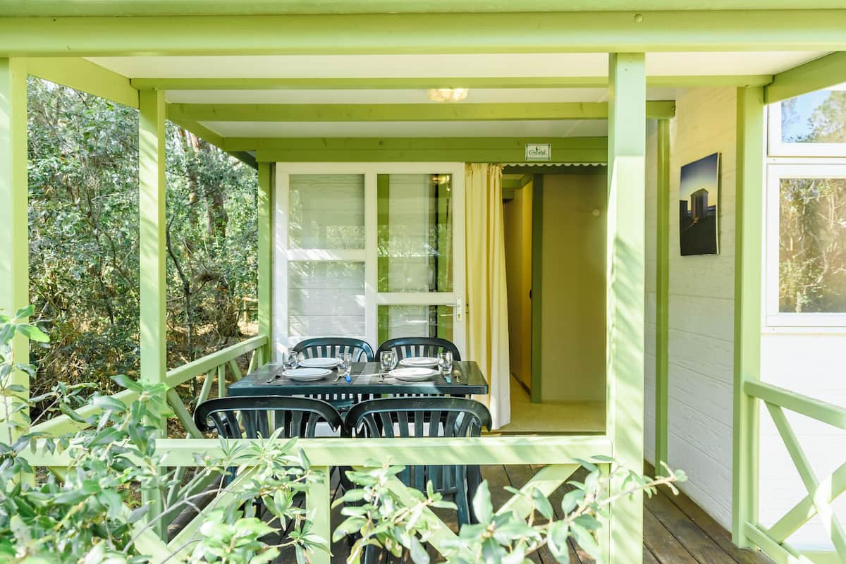 A covered outdoor dining area with a table set for four, surrounded by greenery.