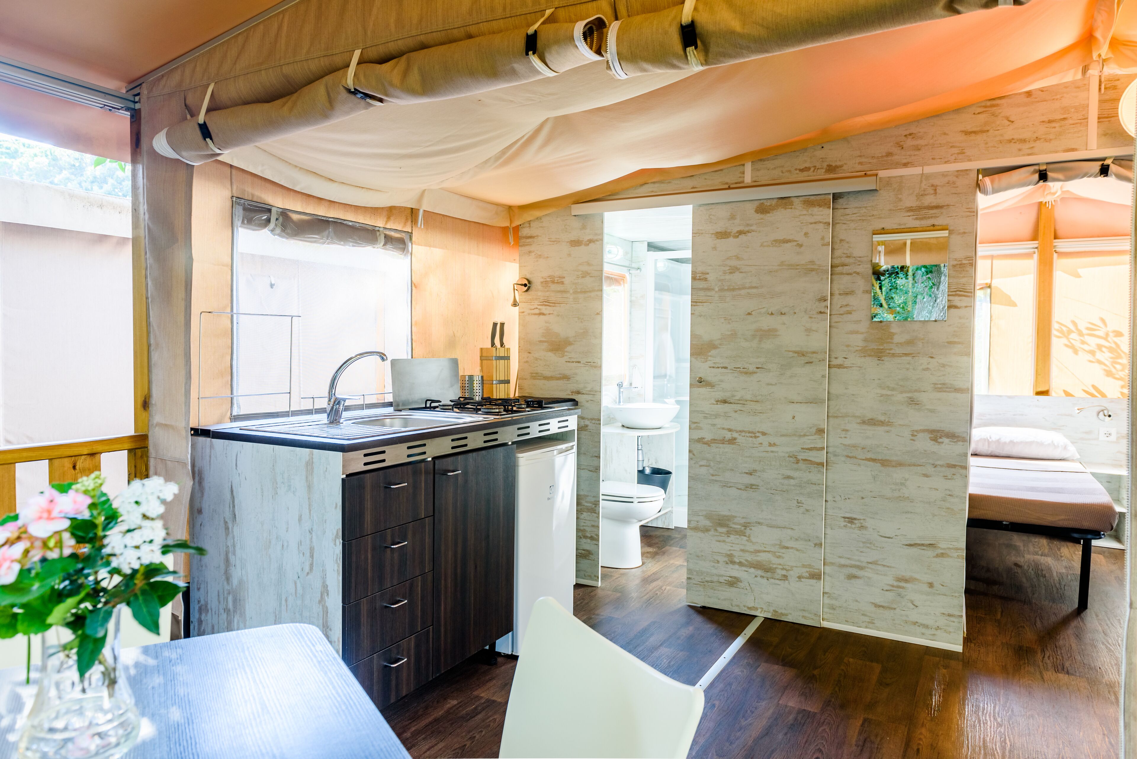 Cocina compacta con lavabo, estufa y refrigerador blanco. Cuenta con comedor con mesa y sillas, y un baño pequeño con inodoro y lavabo.