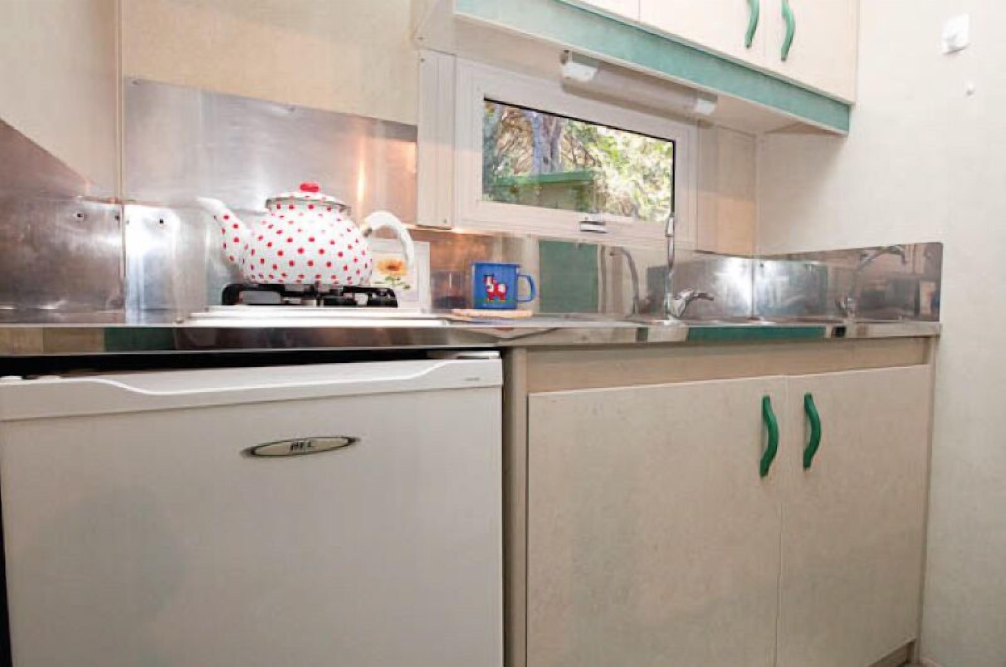 A compact kitchen with a white refrigerator, a stove with a polka-dotted pot, a blue mug, and green cabinets.