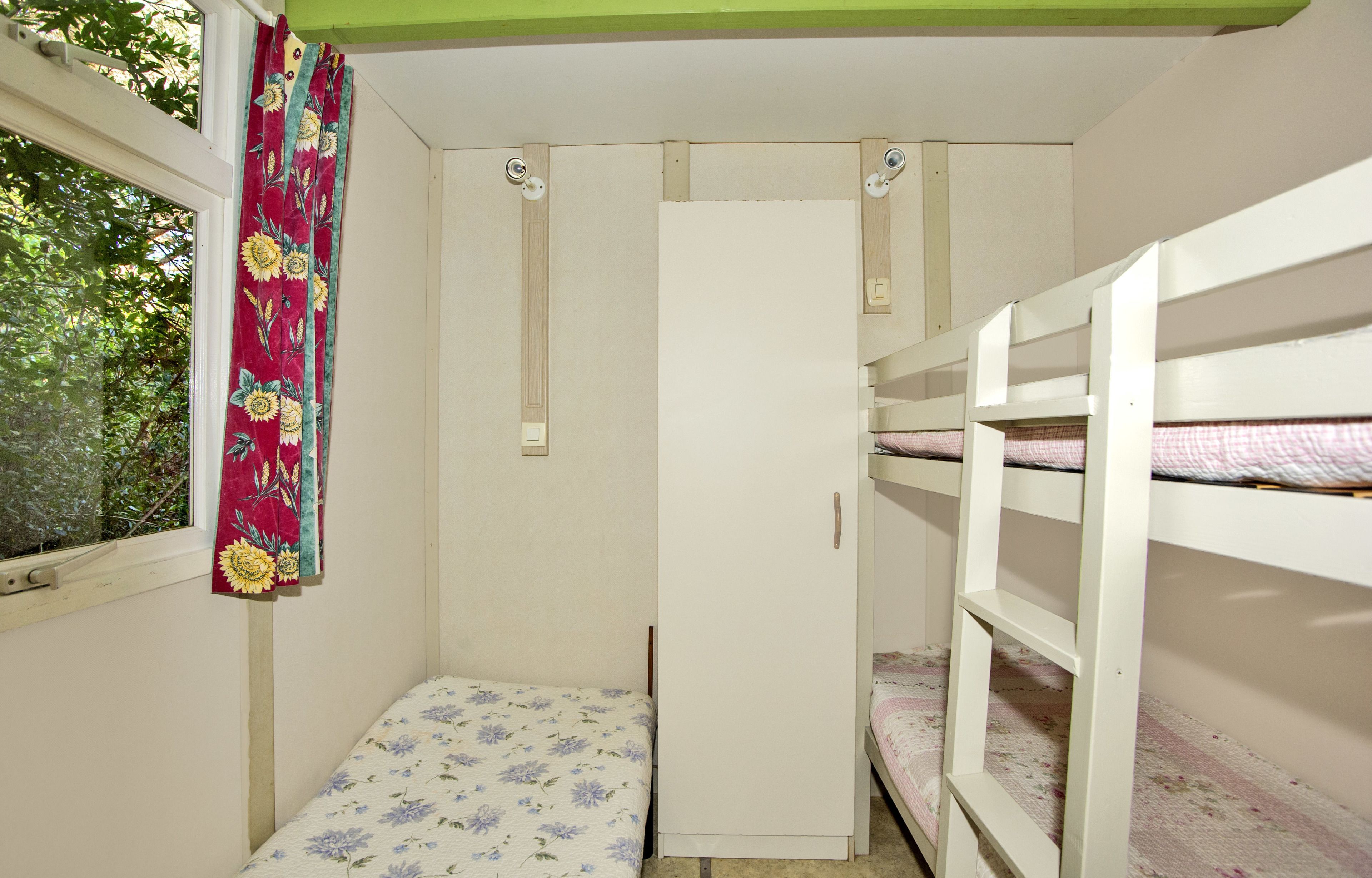 A small, enclosed room with bunk beds, a wardrobe, and a window with a curtain.