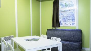 Een kamer met een witte tafel, twee witte stoelen, een donkerblauwe bank en een raam met een zwart gordijn.