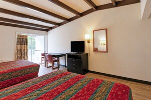 Habitación de hotel con dos camas, un escritorio, un televisor, una silla y un espejo en la pared.