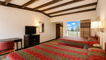 A hotel room with a bed, a desk, a television, and a balcony with a view of trees.