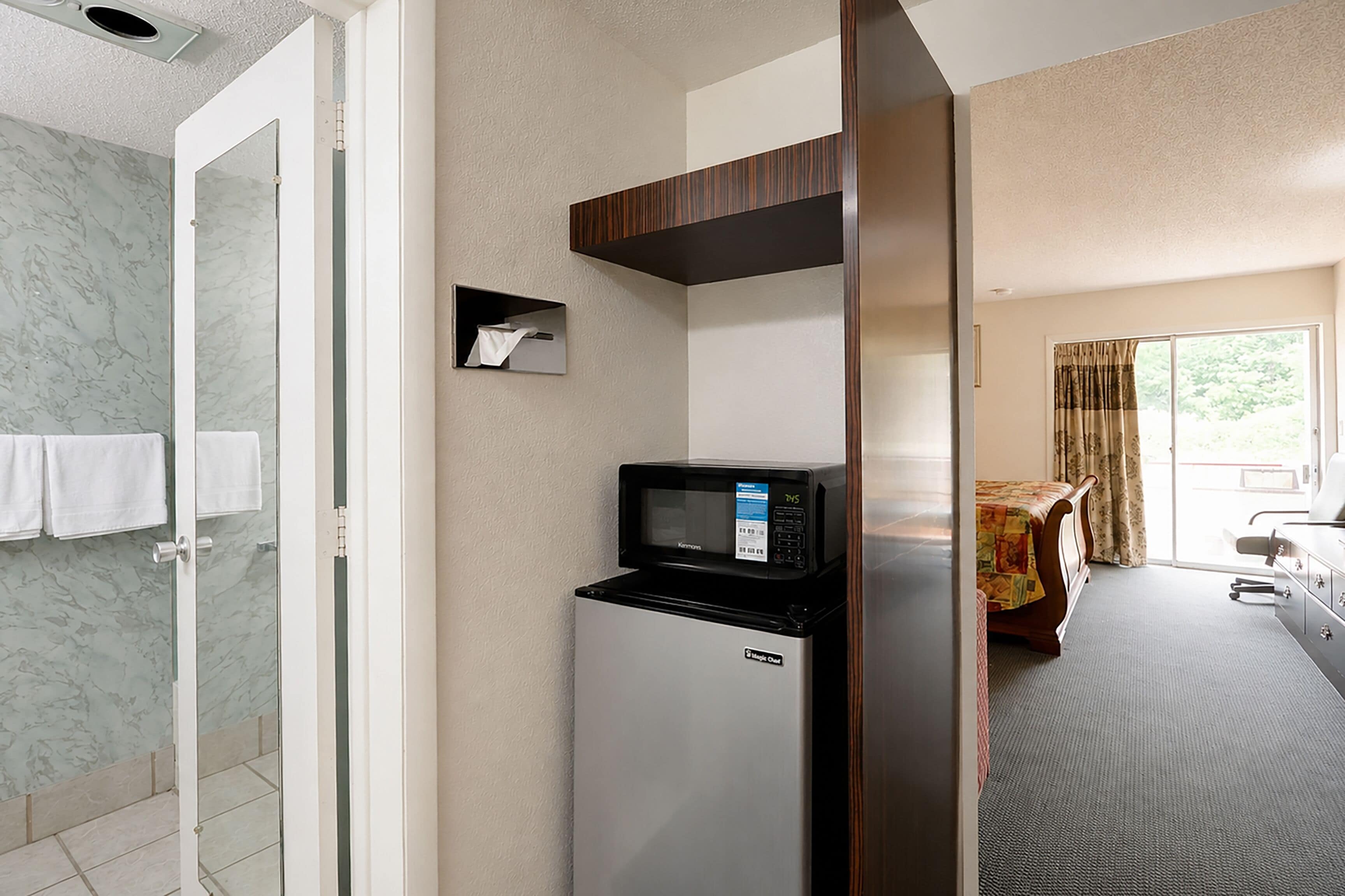 A hotel room with a bathroom, a microwave, and a bed with a window.