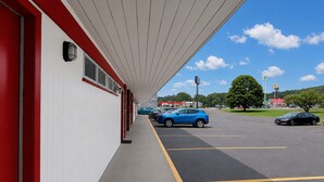 A covered walkway leading to a building with a red and white facade, a parking lot with several cars, and a clear blue sky with clouds. - Hometown Inn Staunton VA near Hwy 11 (Staunton)