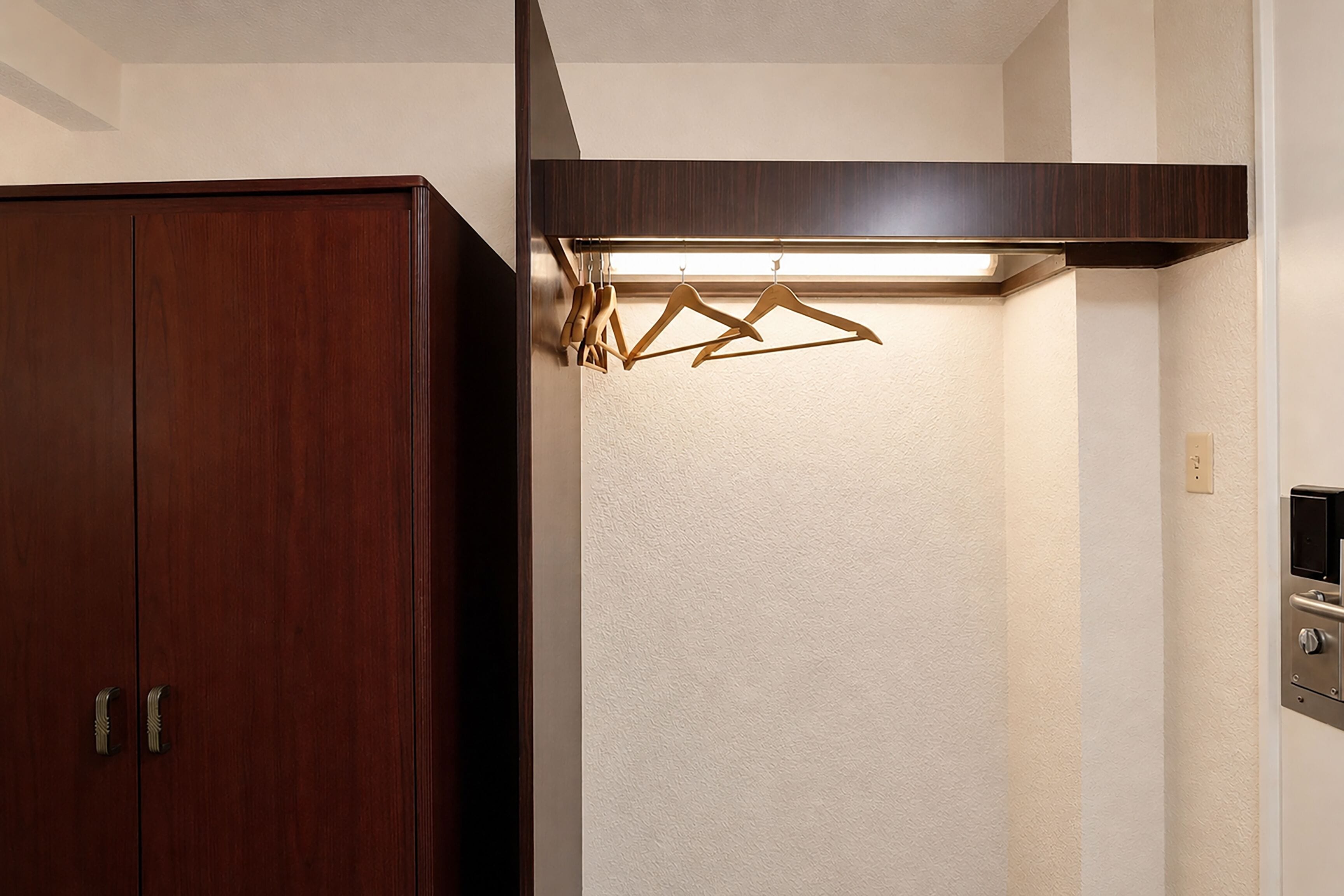 A wooden wardrobe with a mirror, a wall-mounted light fixture, and a door with a handle.