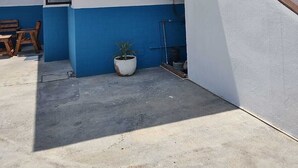 A small, enclosed outdoor area with a blue and white wall, a wooden bench, a potted plant, and a small window.