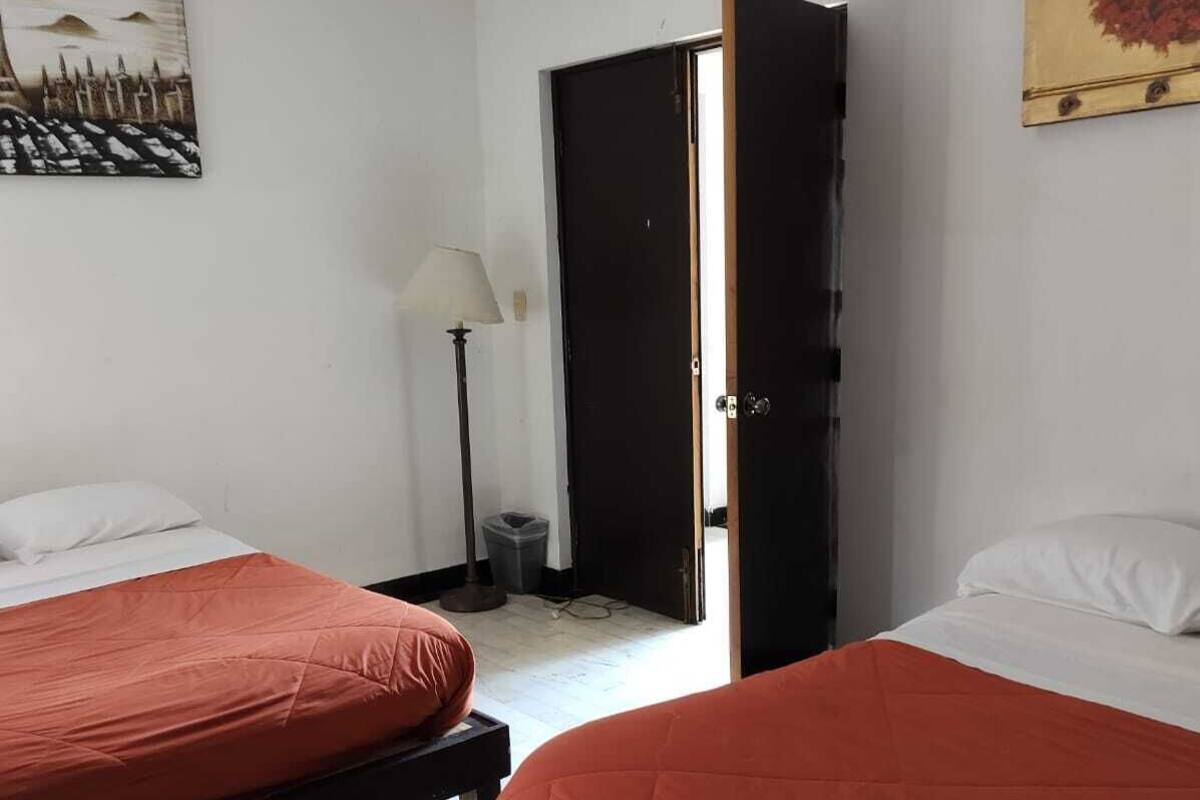 A room with two beds, a door, a lamp, and a painting.
