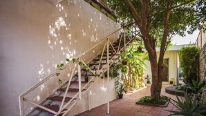 A staircase with a metal railing, surrounded by potted plants and trees, leading to a covered area with a tiled floor.