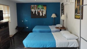A room with two beds, a desk, a chair, a TV, and artwork on the walls.