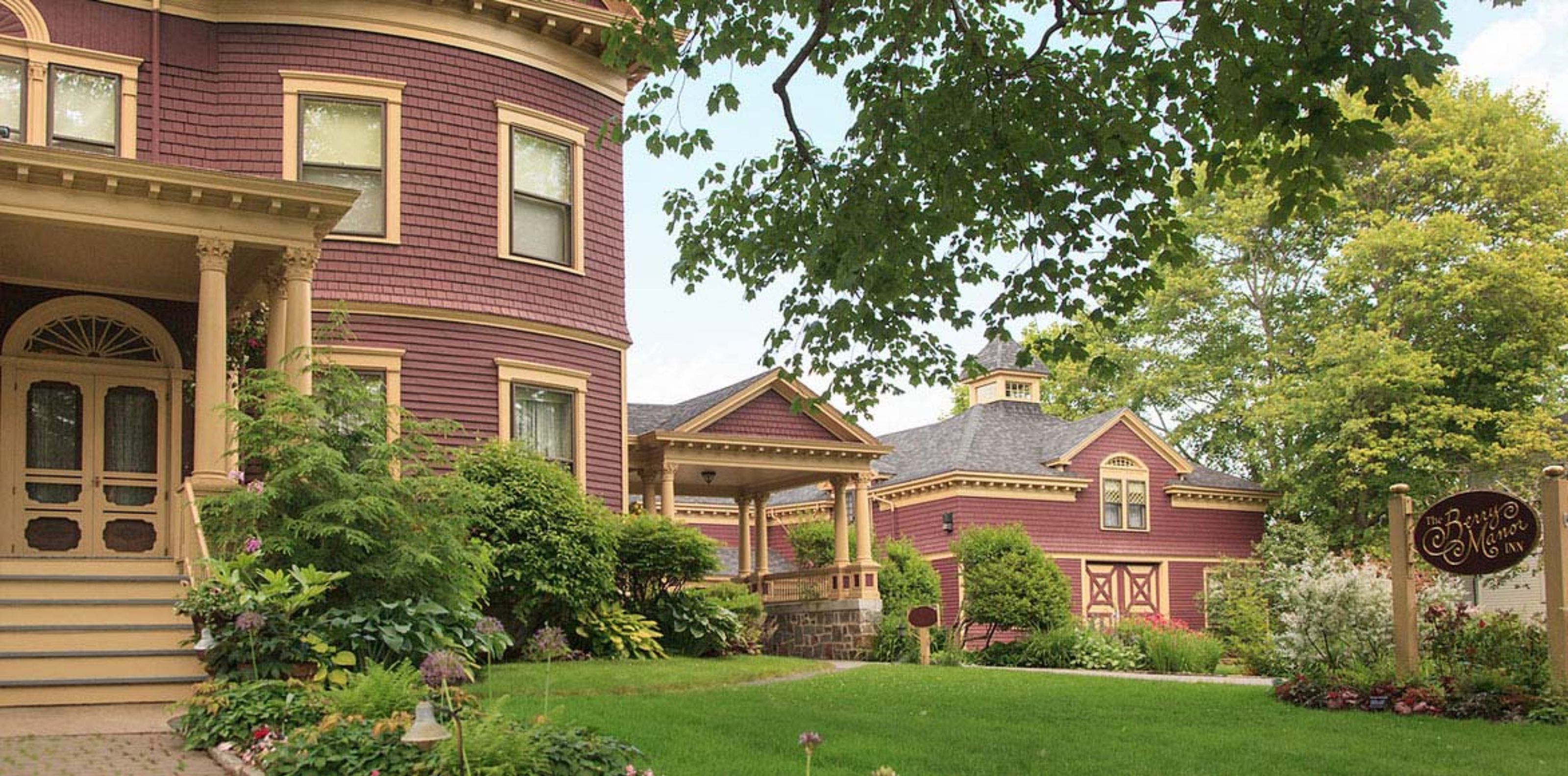 A Victorian-style building with a wrap-around porch, a well-maintained garden, and a sign indicating it is a hotel.