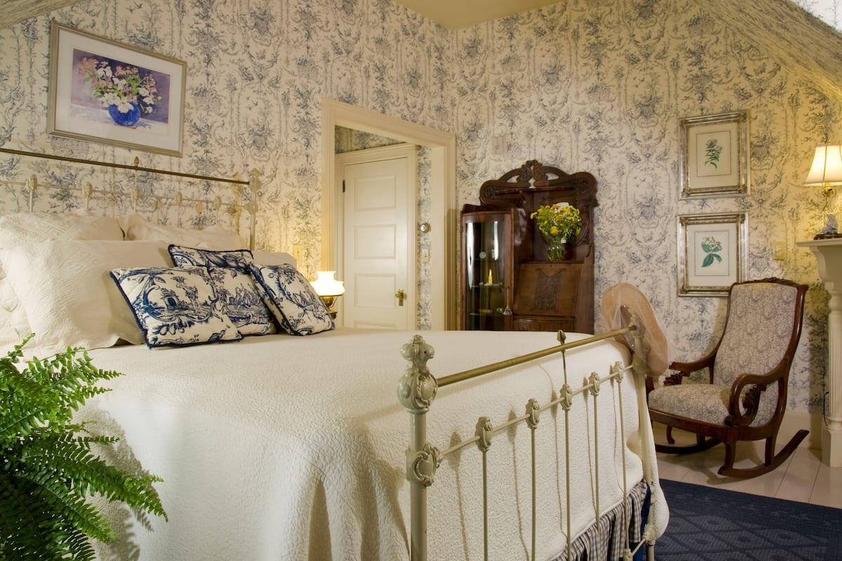 A bedroom with a bed, a rocking chair, a door, and a wall with framed pictures.