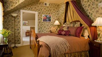 Una camera da letto con un letto a baldacchino, un comodino con una lampada, un tavolino da notte con un vaso di fiori e una porta con uno specchio e un quadro incorniciato.