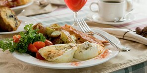 A breakfast plate with eggs, potatoes, tomatoes, and parsley, accompanied by a glass of red drink and a cup of coffee.