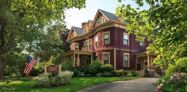 A large, two-story house with a wrap-around porch and a flag in front.