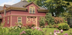 A two-story house with a gabled roof, a front porch, and a garden with various flowers.