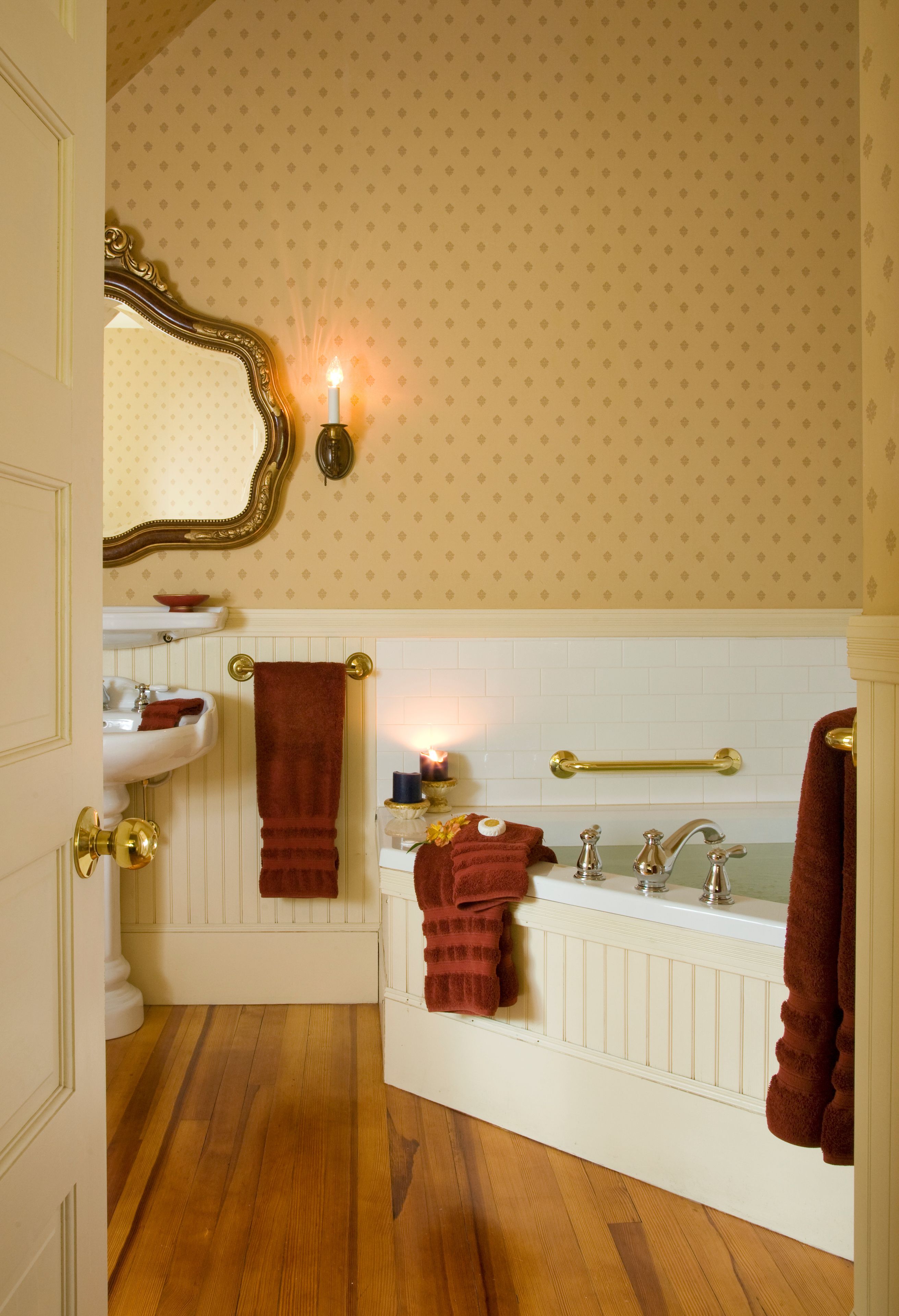 A bathroom with a white bathtub, a sink, and a mirror with a gold frame. There are towels hanging on the wall and a candle on the sink.