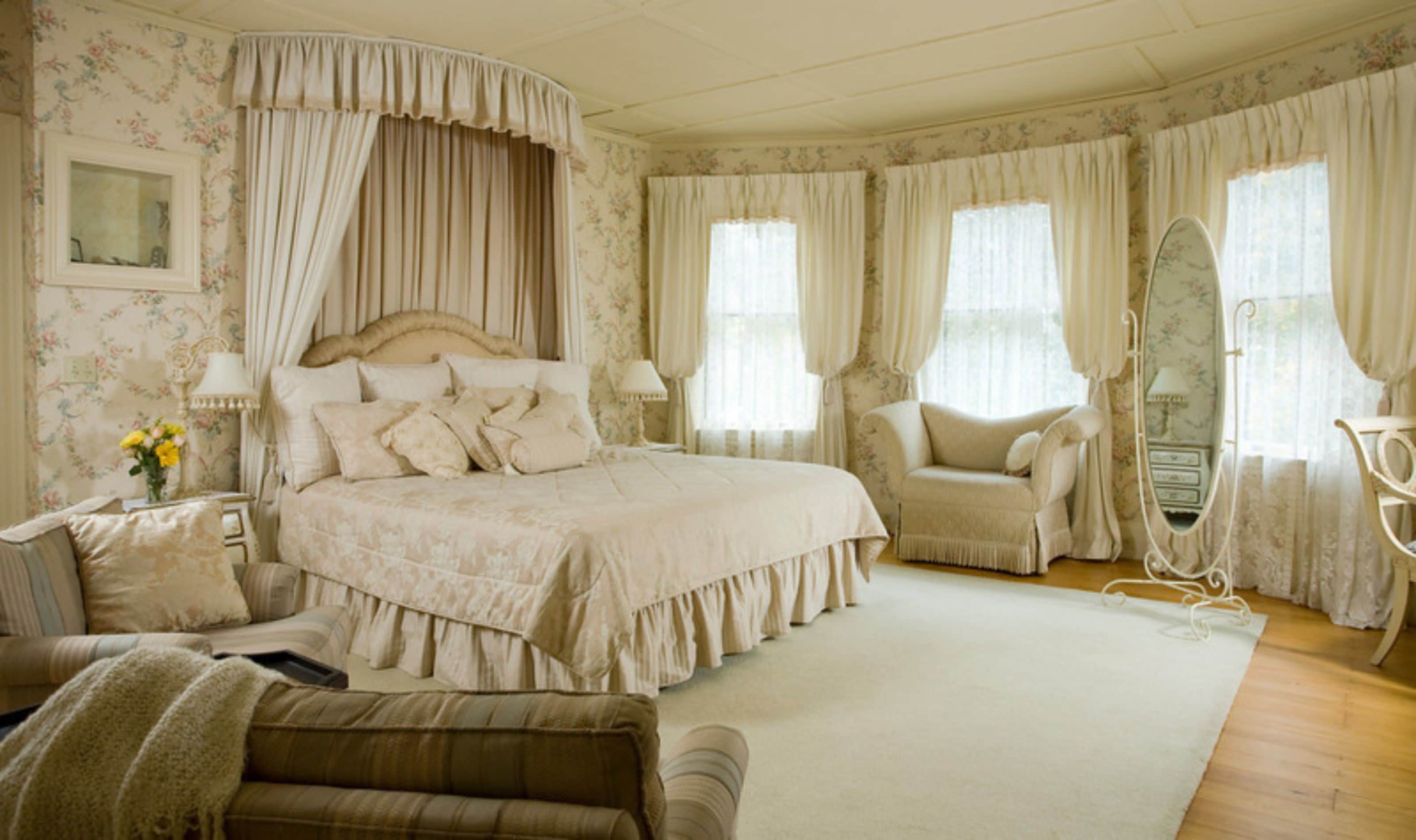 Une chambre classique avec un grand lit, un coin salon avec un fauteuil et une coiffeuse avec un miroir.