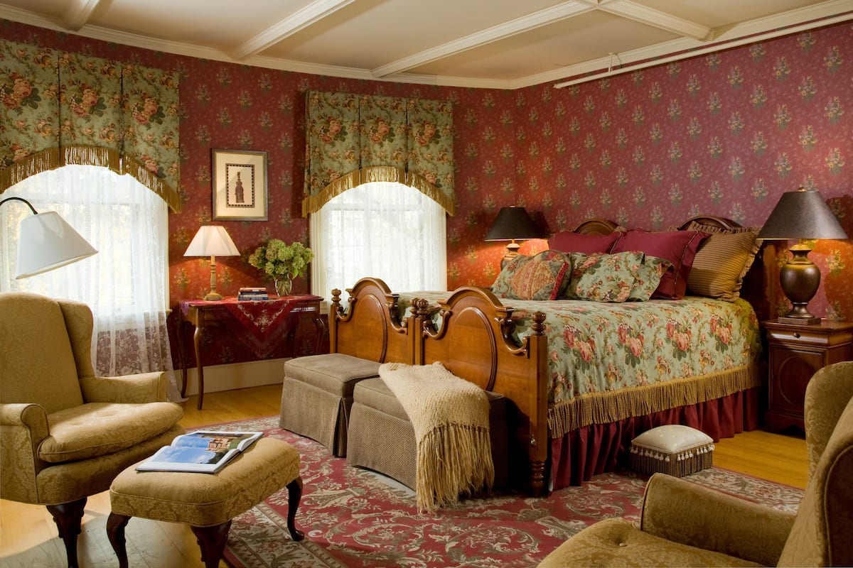 A traditional bedroom with a four-poster bed, two bedside tables, a chair, and a reading area with a book and magazine.