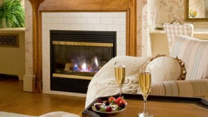 A cozy living room with a fireplace, a sofa, and a table with a fruit platter and champagne glasses. - Berry Manor Inn (Rockland)