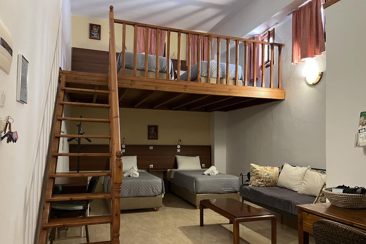 Una habitación tipo loft con una escalera de madera que lleva a una cama individual, un sofá y una mesita.