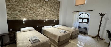 Habitación de hotel con tres camas, una pared de piedra, un equipo de aire acondicionado, una ventana con vistas y un perchero.
