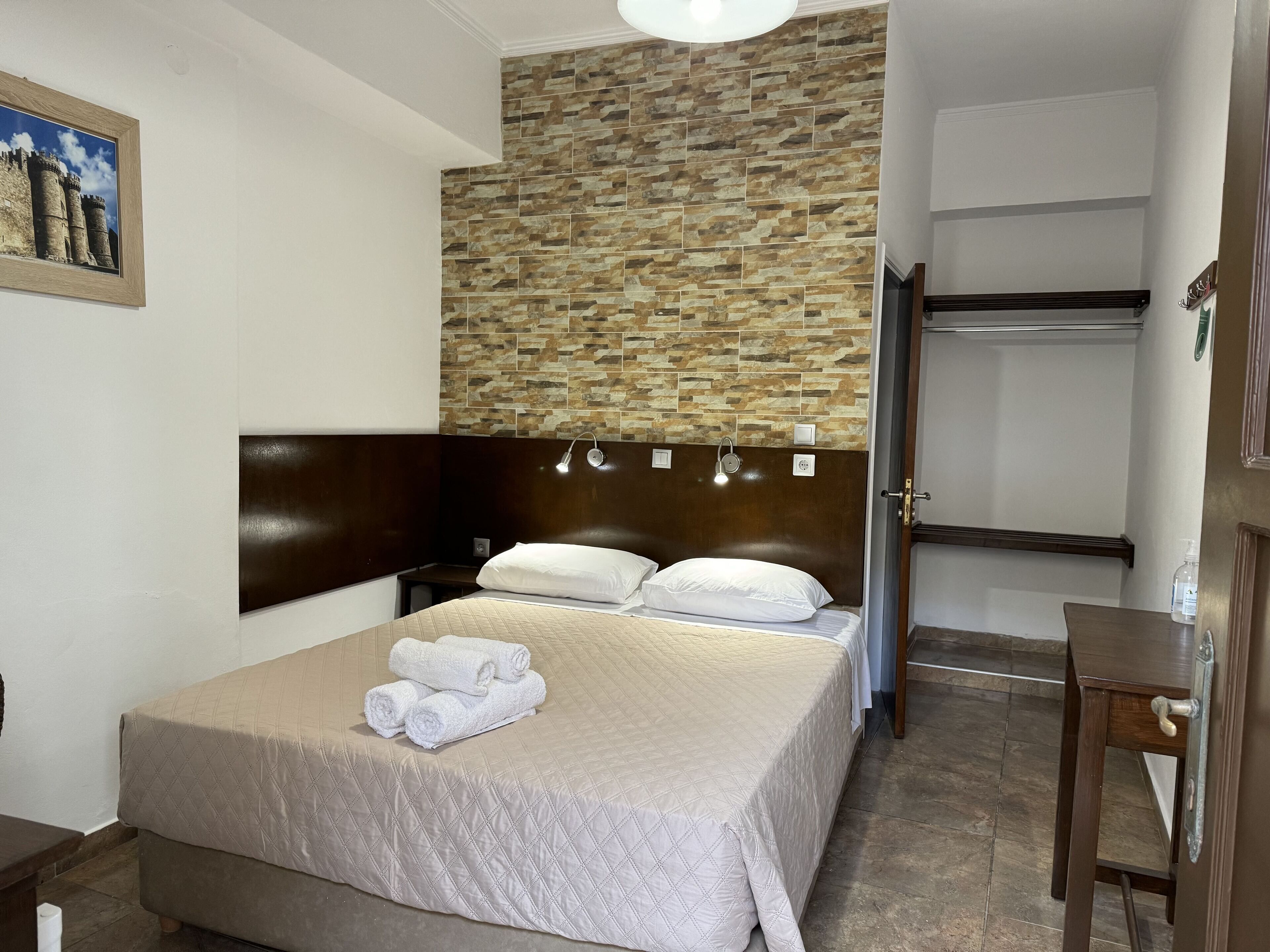 Habitación de hotel con una cama, cabecera, pared con diseño similar a piedra, un cuadro en la pared y una puerta que da a otra habitación.