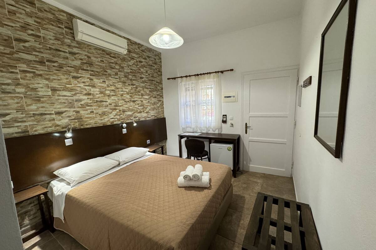 Habitación de hotel con cama, escritorio, silla, refrigerador pequeño y puerta.
