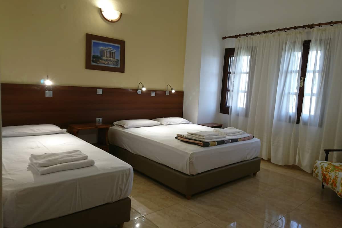 Habitación de hotel con dos camas, cabecero de madera, un cuadro enmarcado en la pared y una ventana con cortinas traslúcidas.
