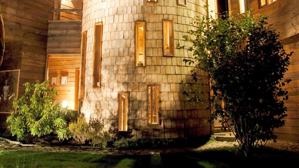 Uma torre cilíndrica com várias janelas, rodeada por edifícios de madeira e um jardim.