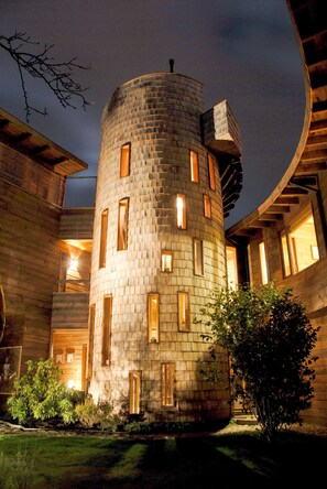 Una torre cilíndrica con múltiples ventanas, rodeada de construcciones de madera y un jardín.