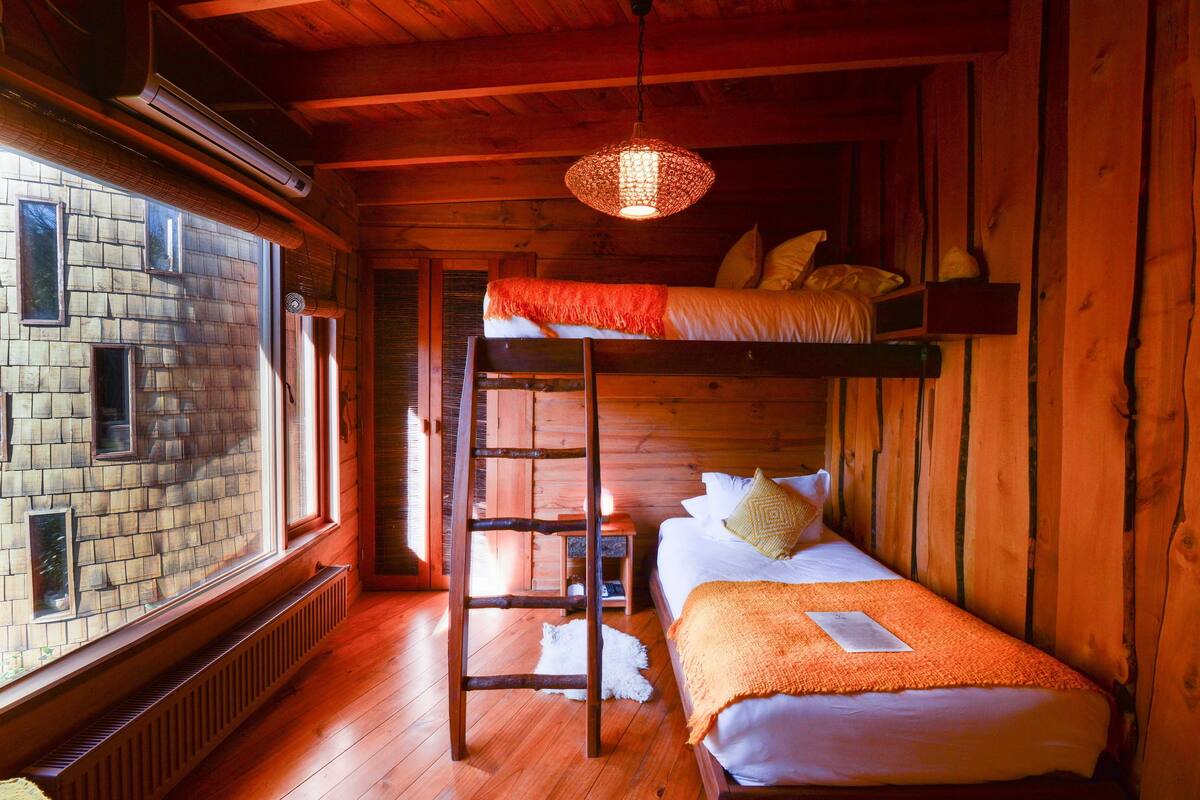 Una habitación de cabaña de madera con literas, una escalera, una ventana y una lámpara colgante.