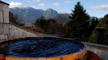 Un jacuzzi con revestimiento de madera, rodeado por una terraza de madera, con montañas al fondo.