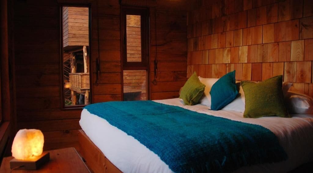 Un dormitorio de cabaña de madera con cama, almohadas y una lámpara de sal.