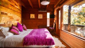 Quarto de cabana de madeira com uma cama, travesseiros, um cobertor e uma janela com vista para árvores.