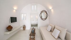 A minimalist room with a white sofa, a wooden table, a TV, and a mirror. - Morfi Cave House (Santorini)