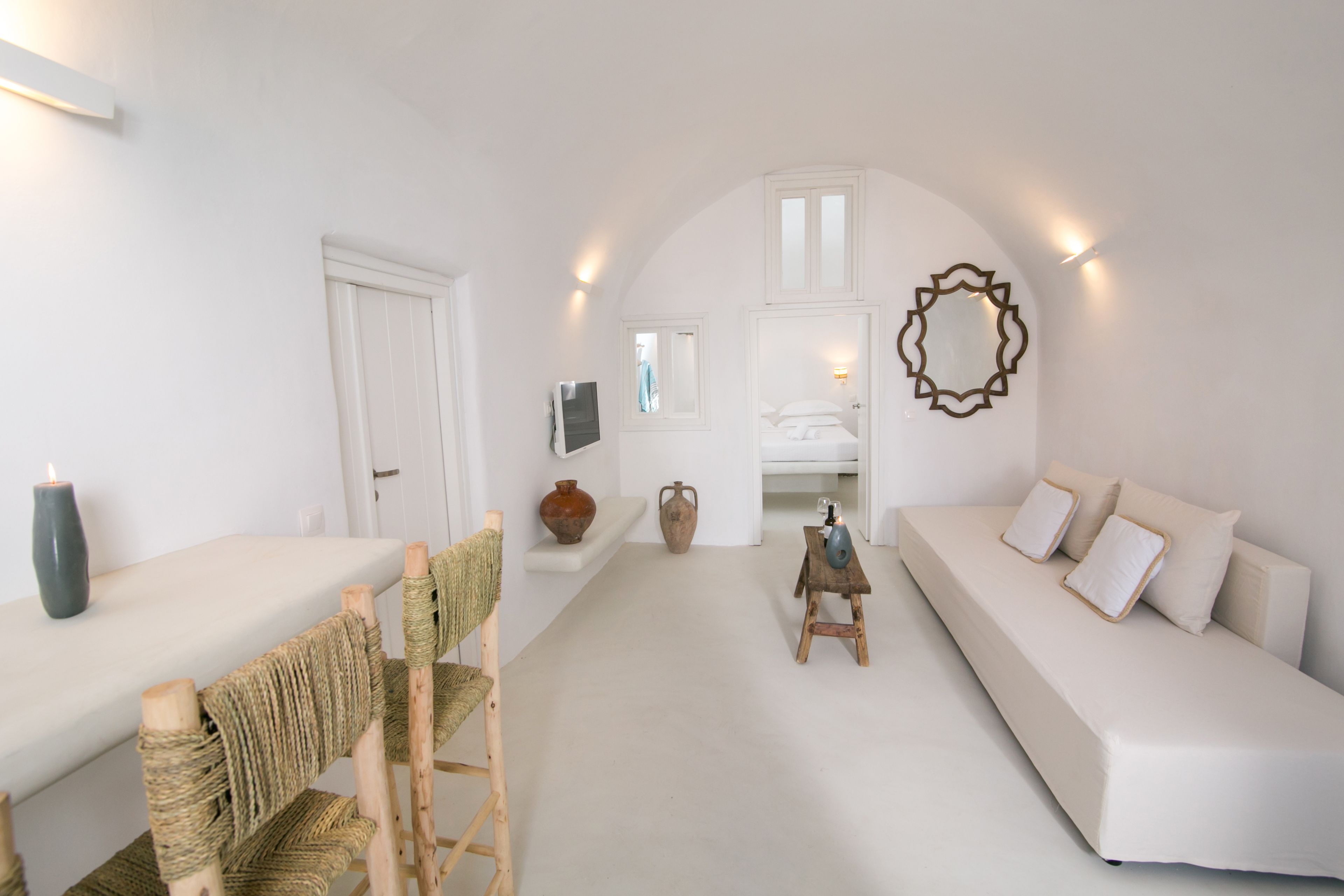 Une pièce au décor minimaliste, avec un canapé blanc, une chaise en bois, une petite table et un téléviseur fixé au mur.