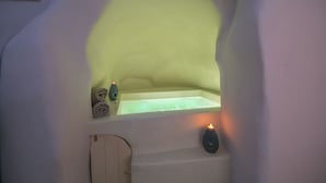 A cozy, dimly lit room with a small window, a bathtub, and a towel rack. - Morfi Cave House (Santorini)